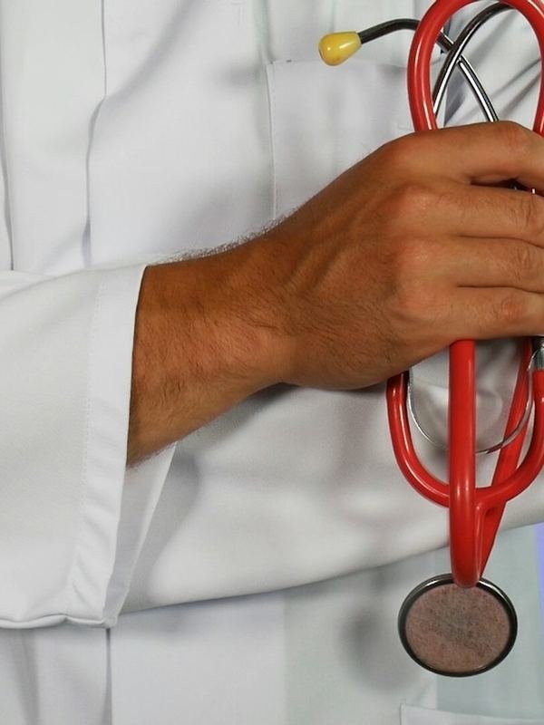 Médico de jaleco segurando o estetoscópio.