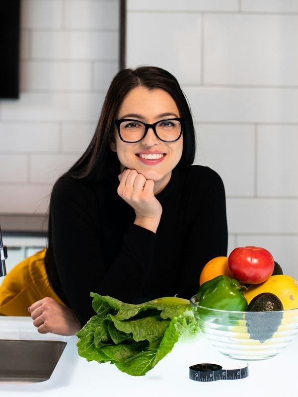 Nutricionista sorrindo ao lado de frutas e verduras.